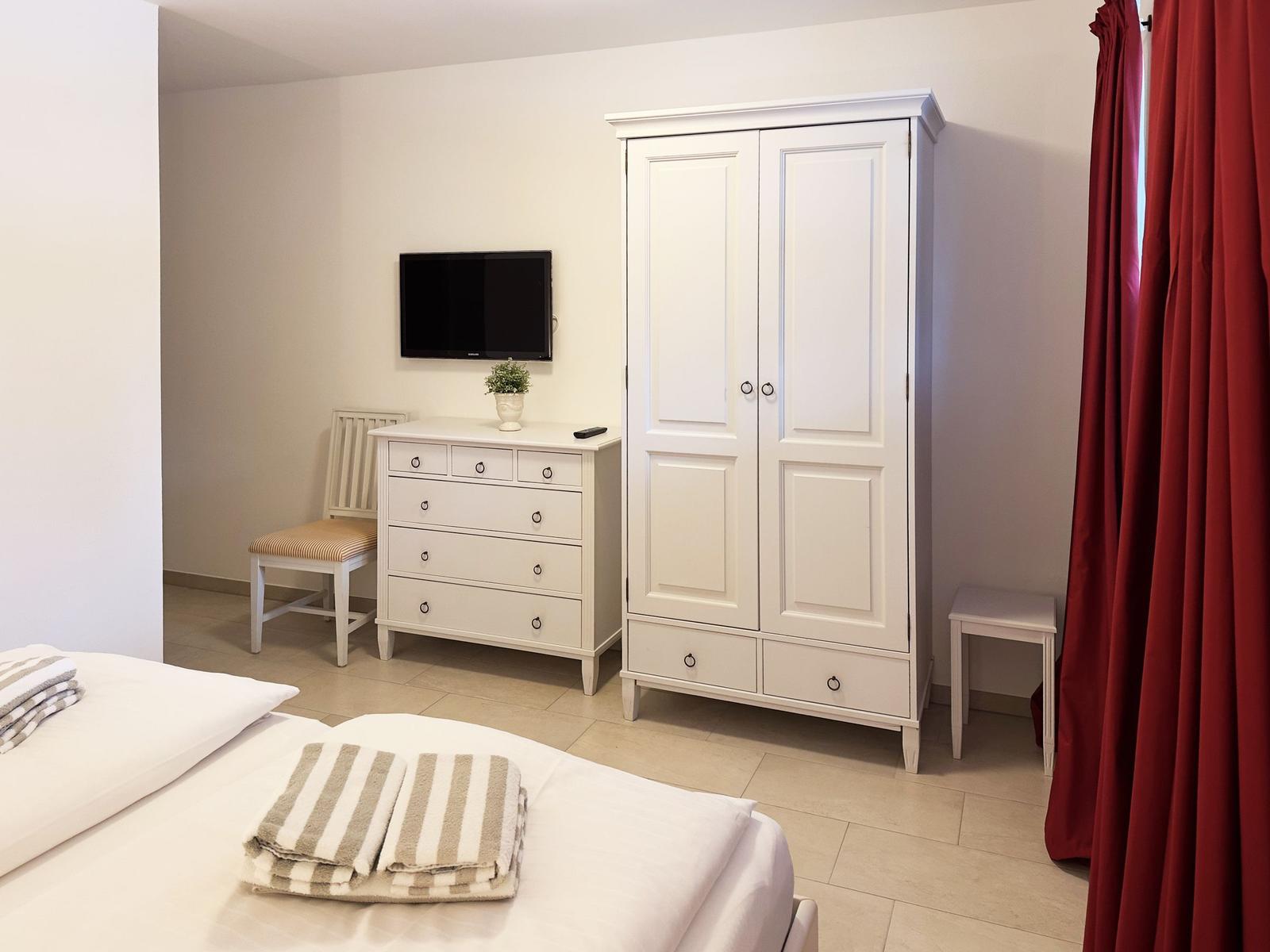 Schlafzimmer mit weißem Kleiderschrank, Schminktisch und Bett mit Handtüchern.
