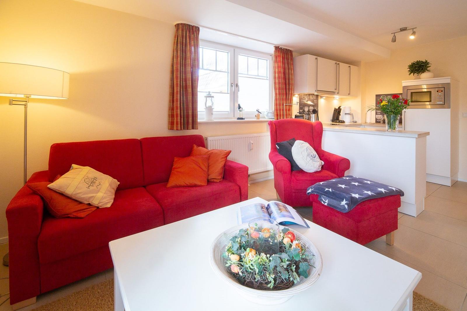 Wohnzimmer mit rotem Sofa, Sessel und Küchenbereich
