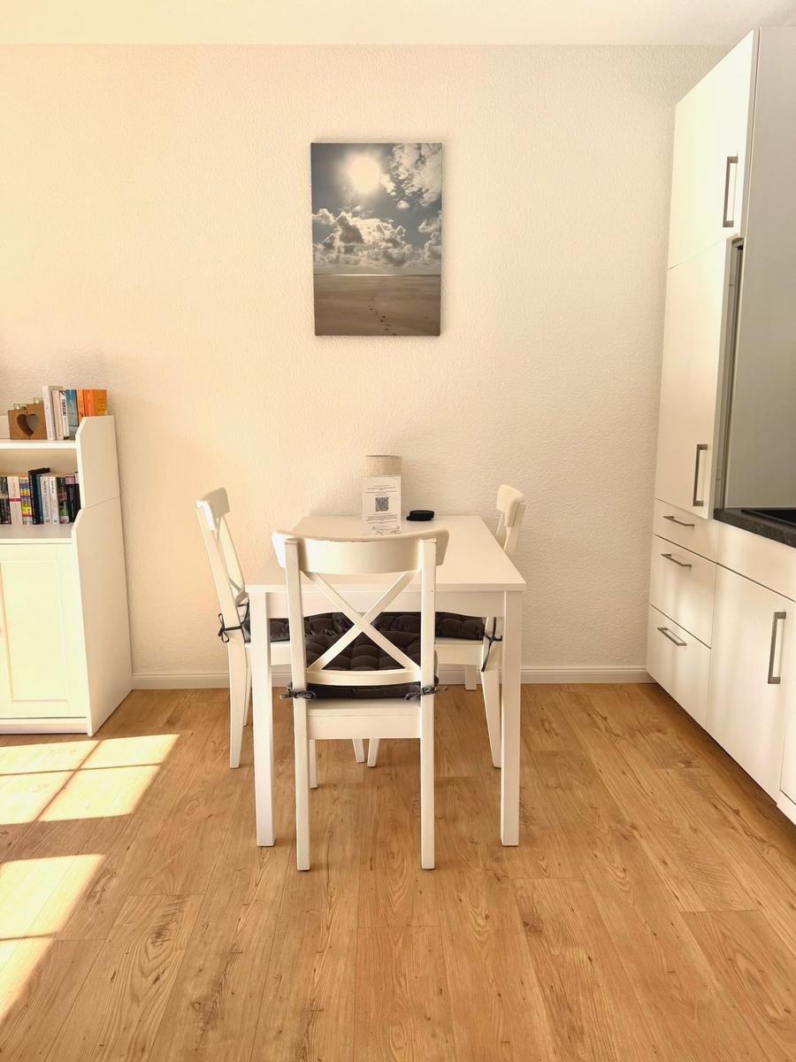 Essbereich mit weißem Tisch und Stühlen, Küchenzeile und Wandbild