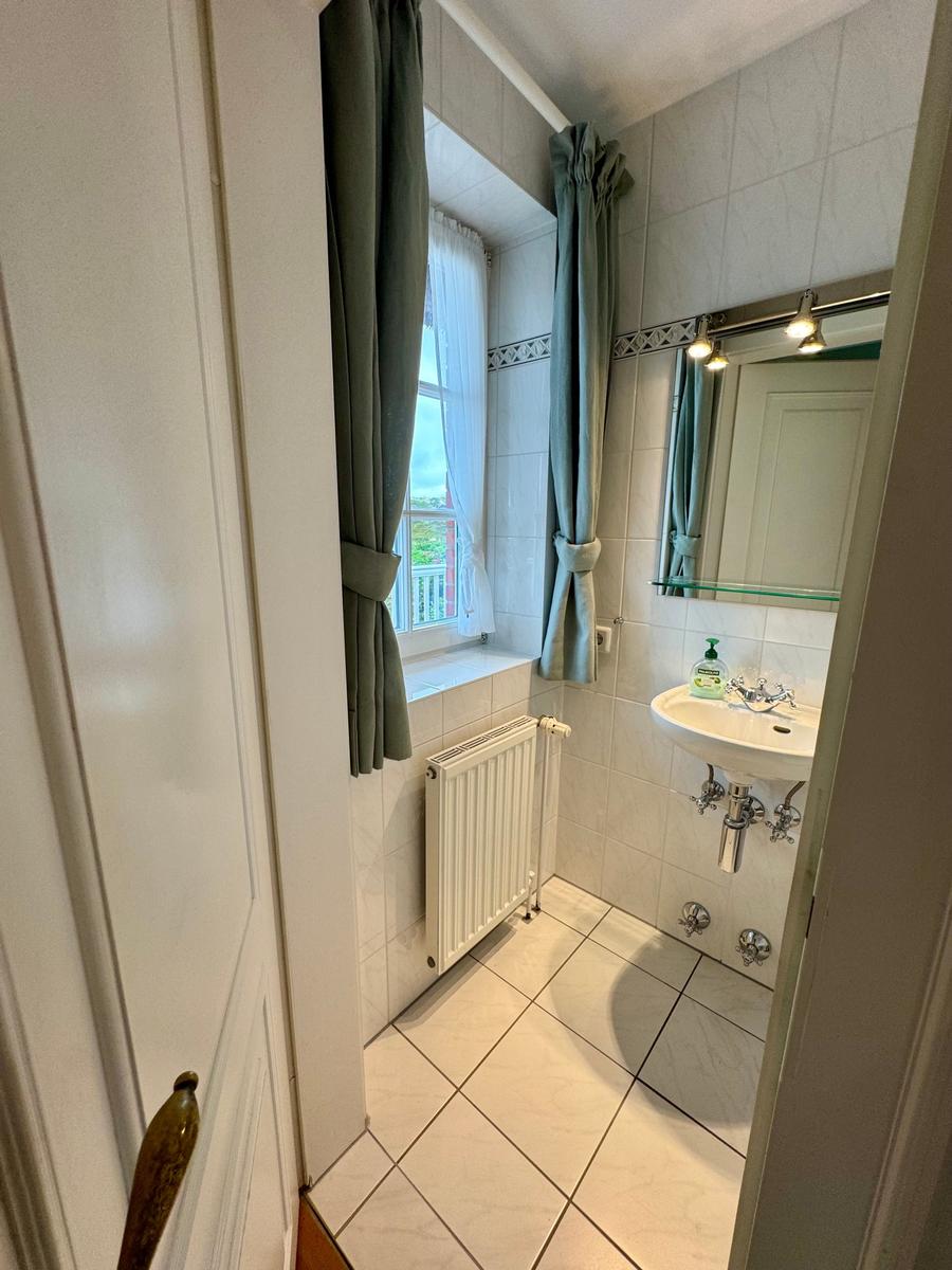 Badezimmer mit Waschbecken, Spiegel, Heizkörper und Fenster mit Vorhängen.