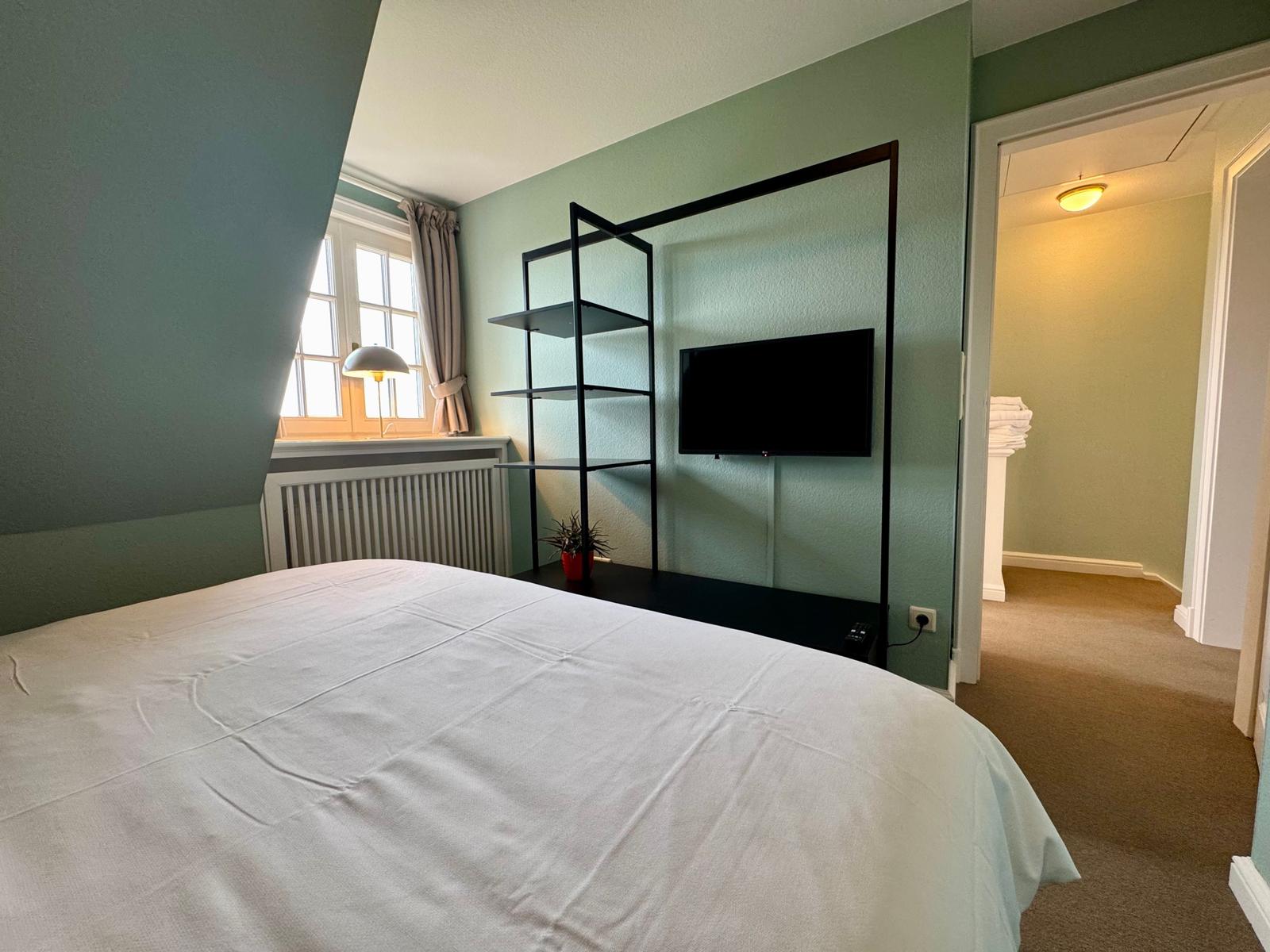 Schlafzimmer mit Bett, Fernseher und Fenster