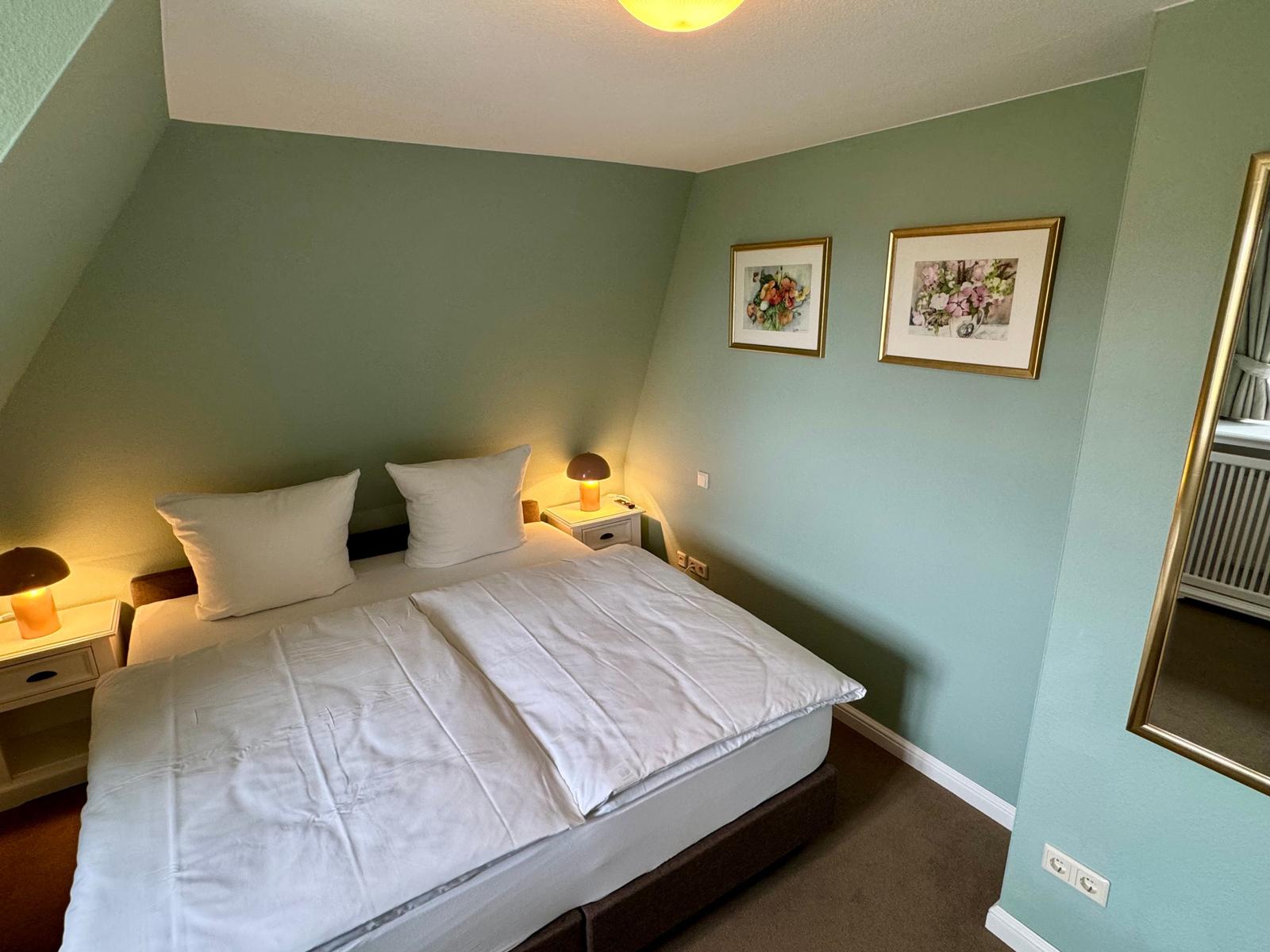Schlafzimmer mit Bett, Nachttischen und Bildern an der Wand.