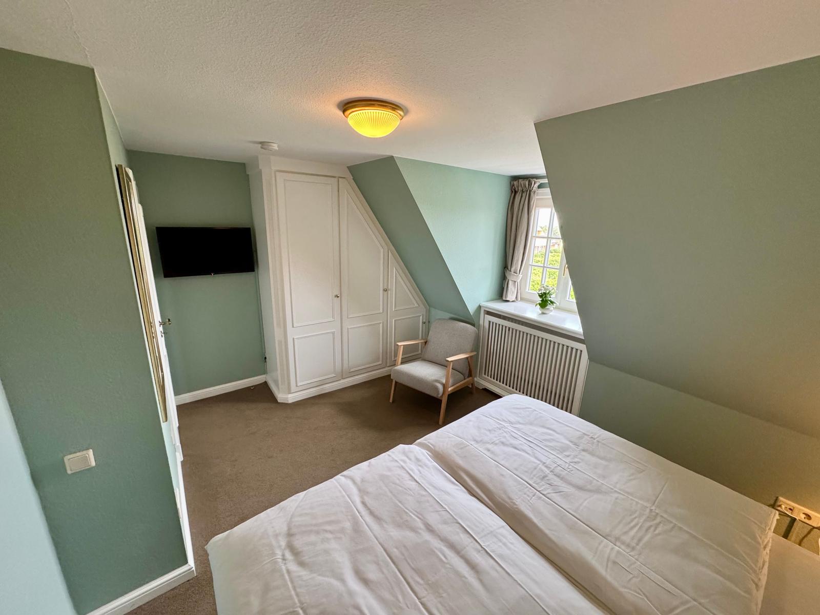 Schlafzimmer mit Dachschräge, Bett, Kleiderschrank und Fenster.