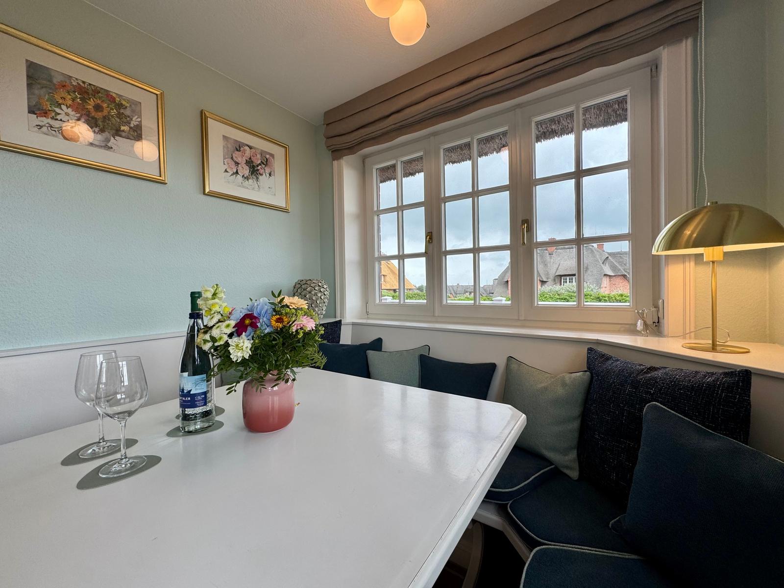 Esszimmer mit Fensterblick, Tisch, Stühle und Blumen.