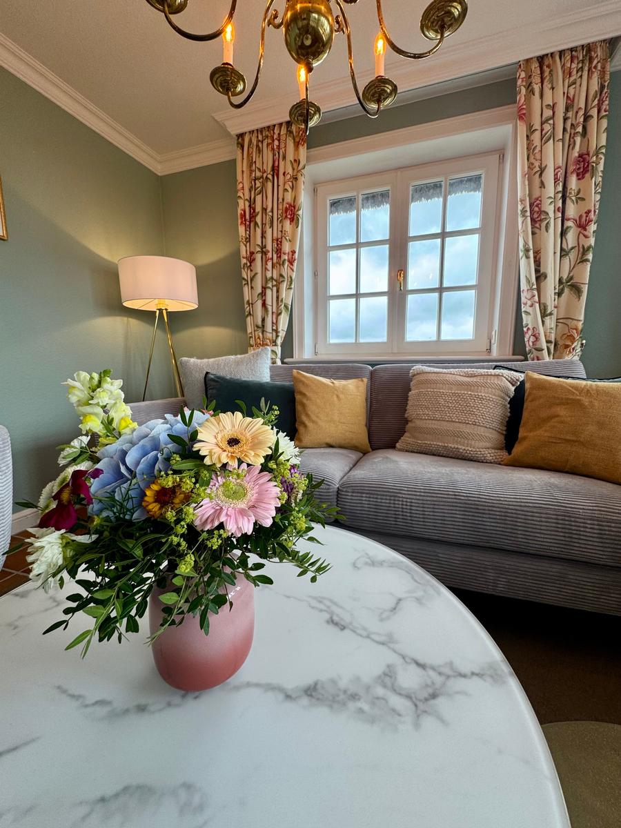 Ein Wohnzimmer mit Sofa, Blumen und Fenster. Die Wände sind hellgrün.