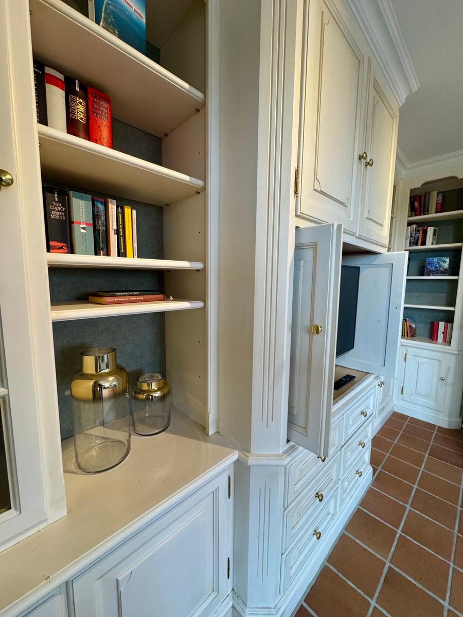 Weißer Schrank mit offenen Regalen, Fernseher und Glasbehältern auf Holzfußboden.