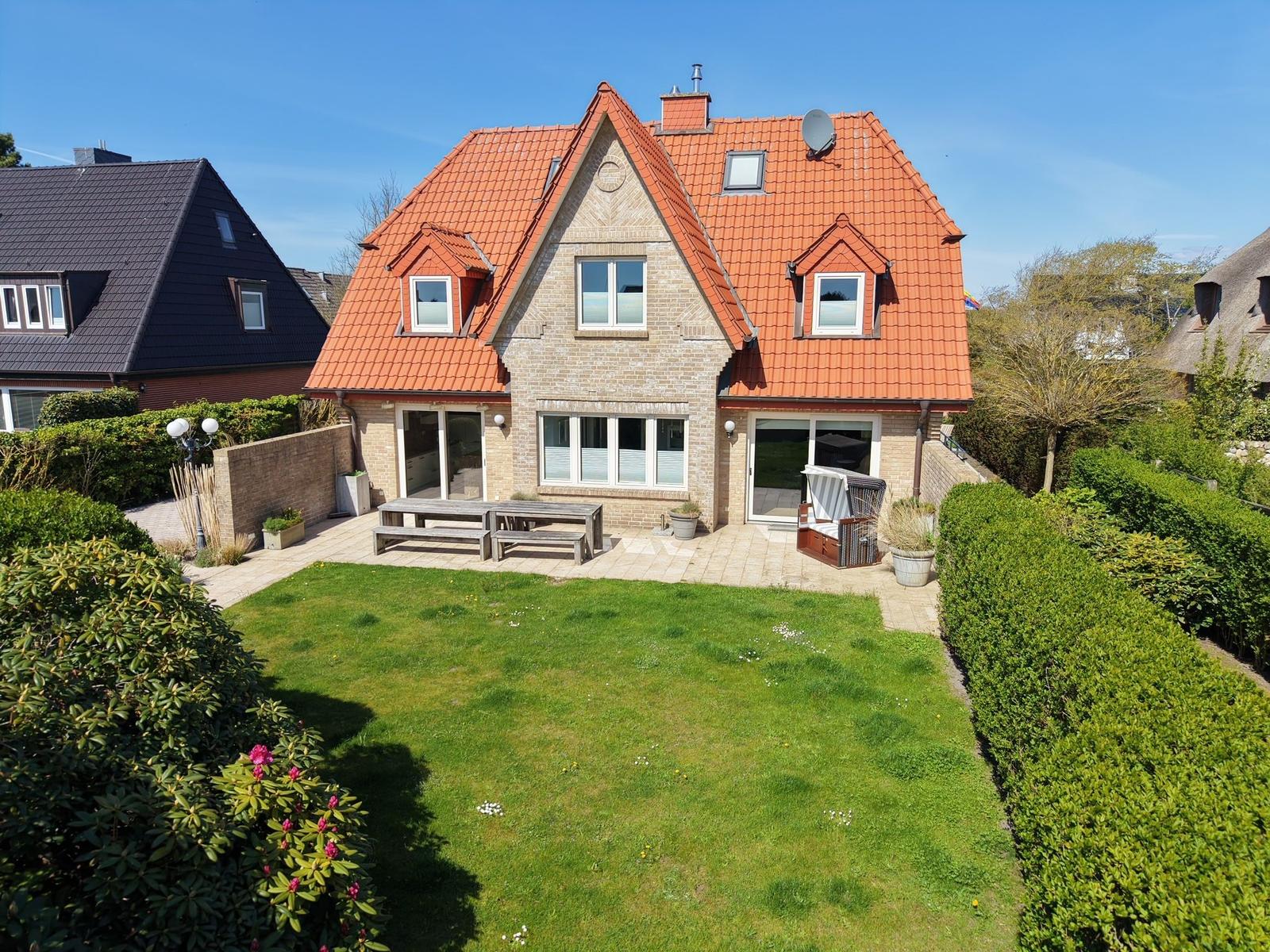 Haus mit rotem Dach, Garten und Terrasse mit Tisch und Stühlen.