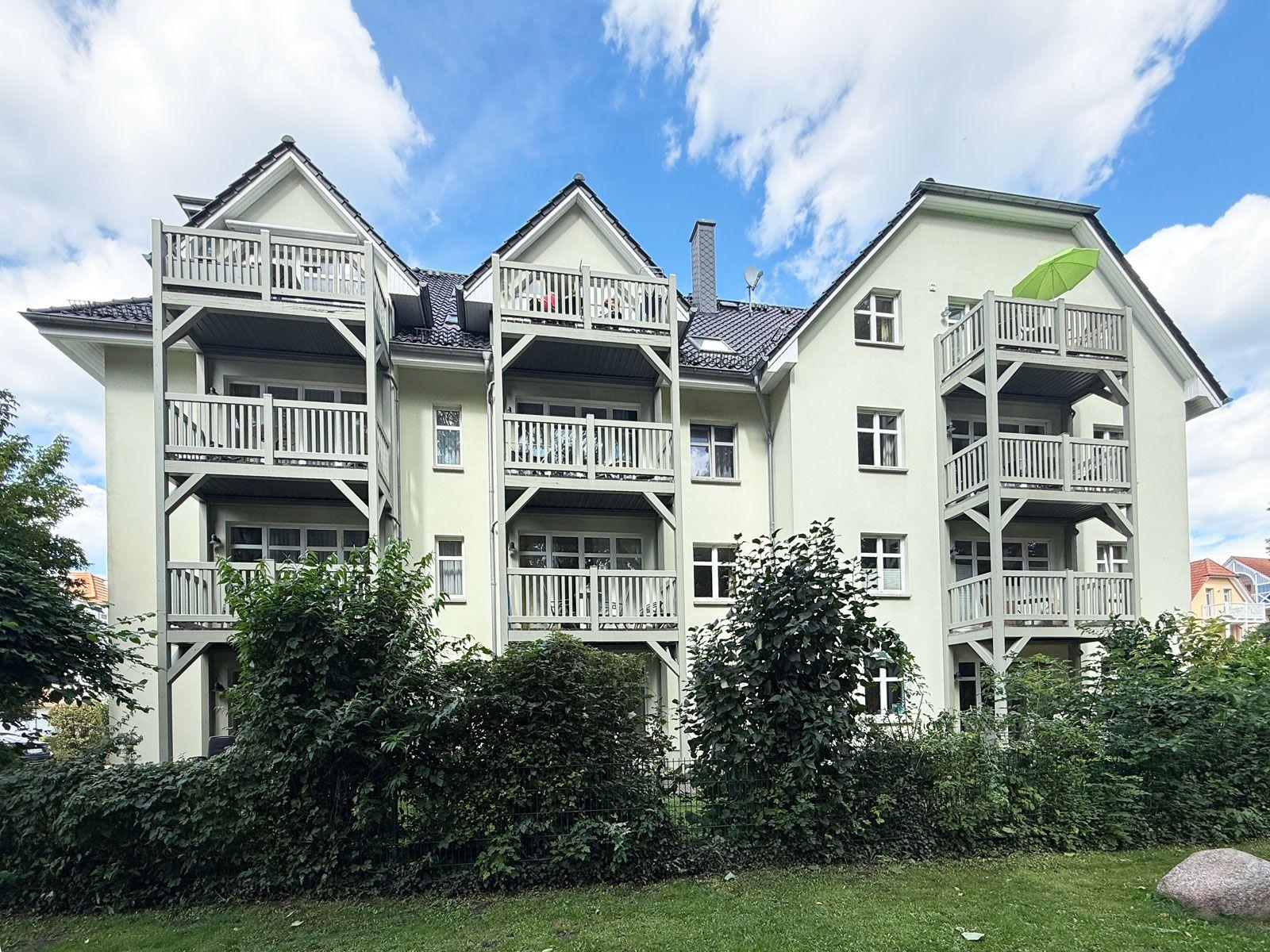 Haus mit mehreren Balkonen und grüner Umgebung unter blauem Himmel.