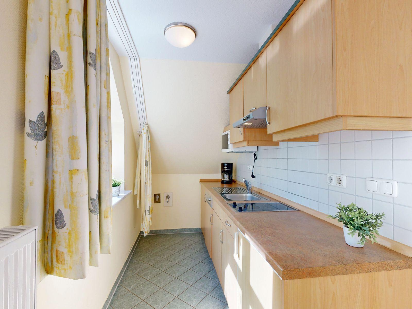 Küche mit Holzschränken, Arbeitsplatte und Fenster mit Vorhängen.