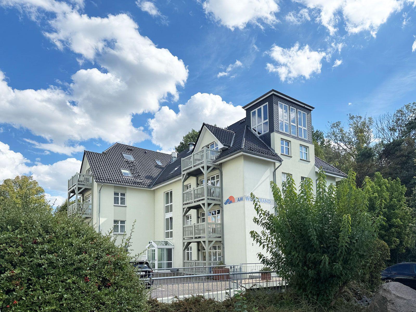 Haus mit Balkonen und Dachterrasse unter blauem Himmel mit weißen Wolken.