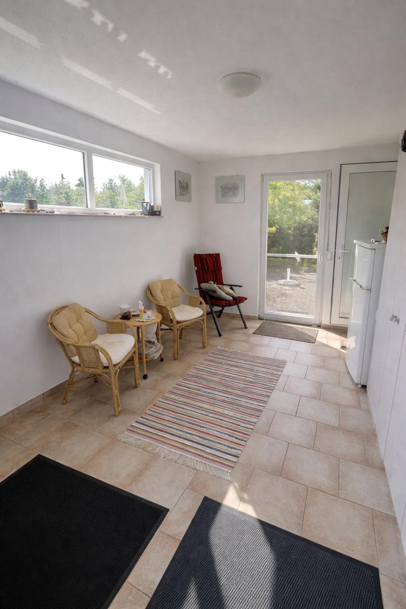 Raum mit Sitzgelegenheiten, Fenster und Glastür zur Terrasse. Fliesenboden und Teppich.
