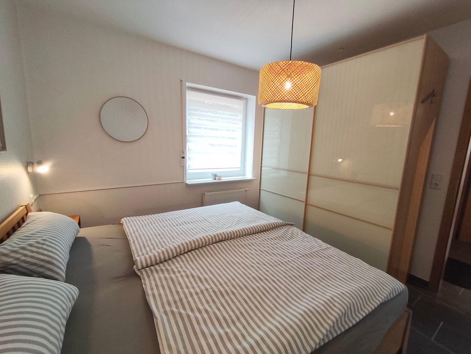 Schlafzimmer mit Bett, Kleiderschrank und Fenster.
