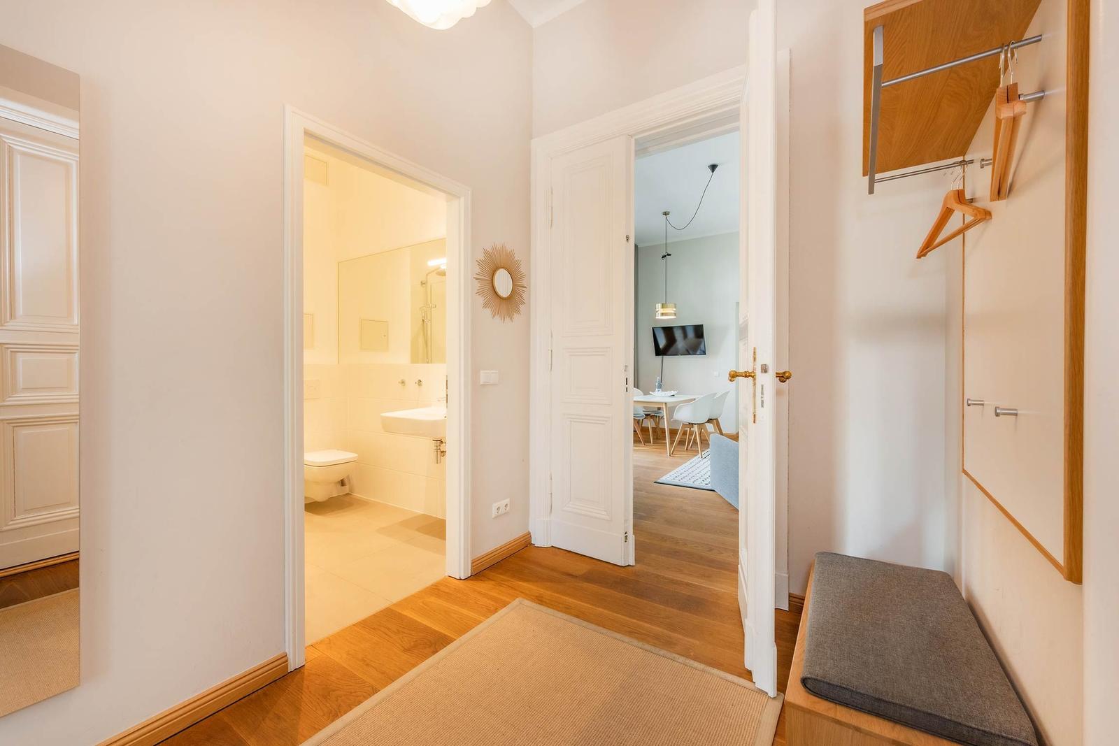 Flur mit Blick in Bad und Wohnbereich, Holzboden und Kleiderschrank mit Haken.