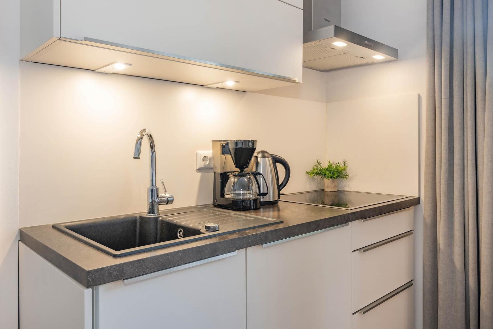 Küche mit Spüle, Kaffeemaschine und Kanne auf dunkler Arbeitsplatte.