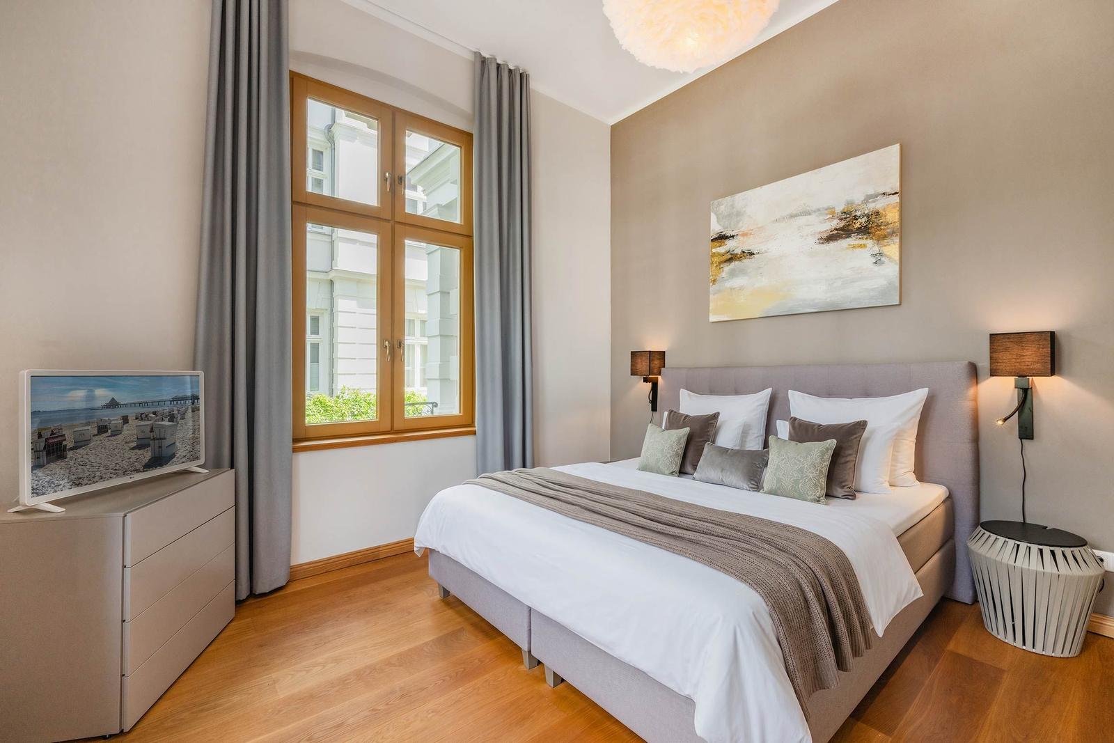 Schlafzimmer mit Bett, Fenster und TV. Holzboden und Wandbild.