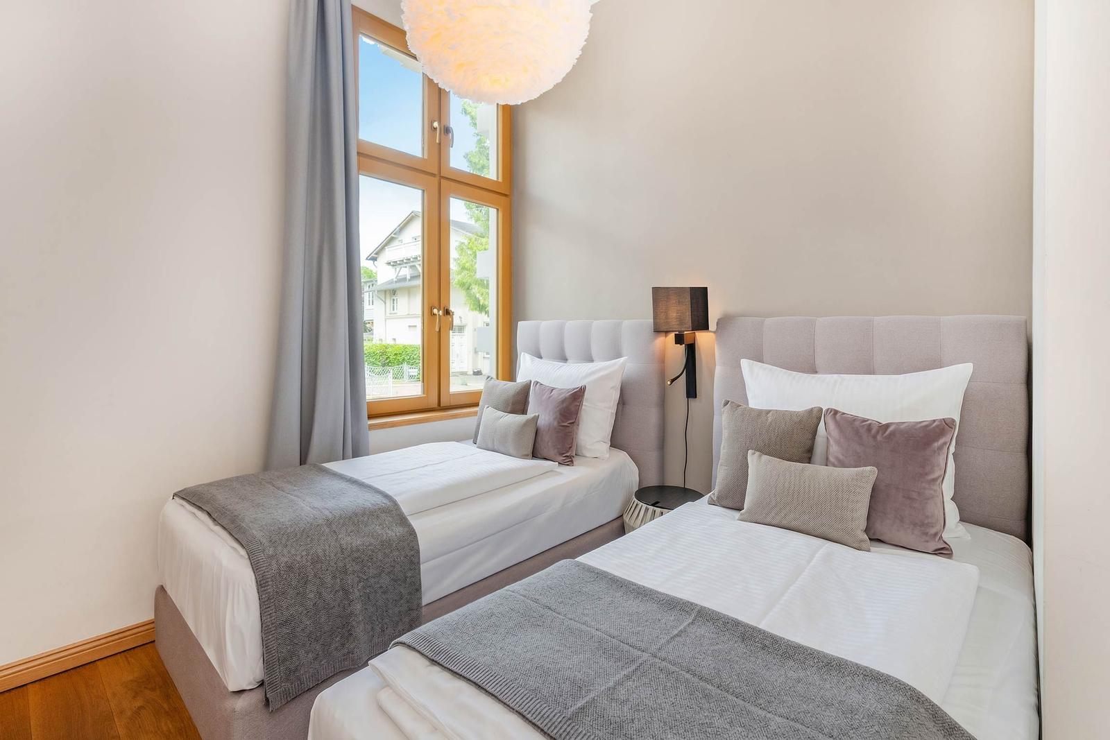 Zwei Betten mit Kissen und Decken. Fenster mit Blick nach draußen.