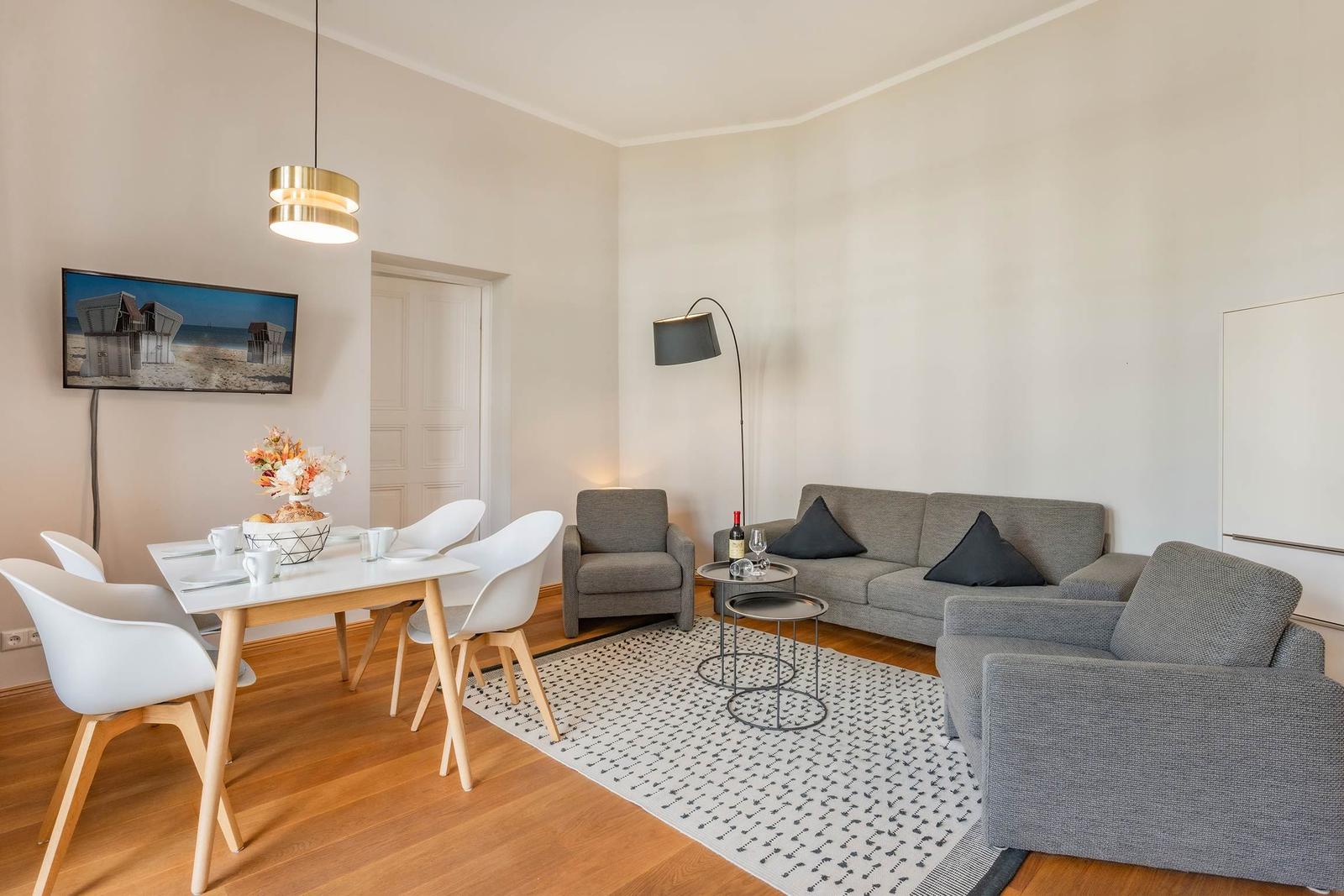 Wohn- und Essbereich mit grauem Sofa, weißen Stühlen und Holzboden.