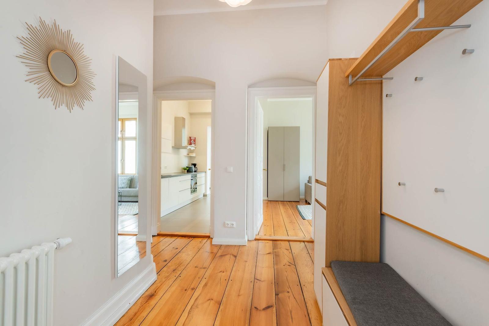 Flur mit Holzboden, Spiegeln und Kleiderschrank. Küche und Schlafzimmer sind sichtbar.