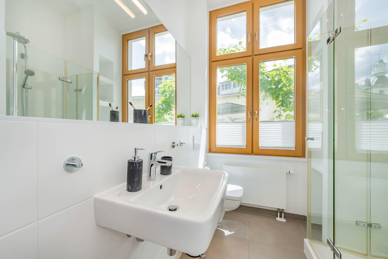 Badezimmer mit Waschbecken, Dusche und Fenster mit Holzrahmen.