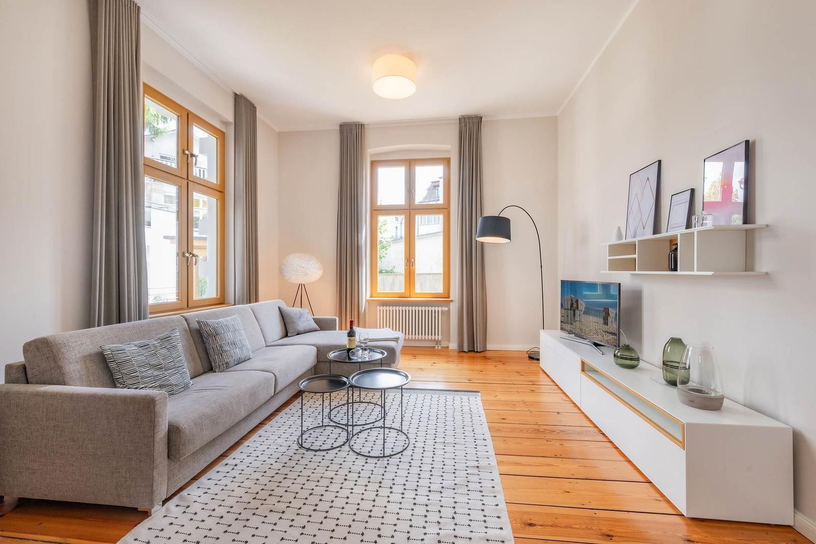 Wohnzimmer mit Sofa, TV und Holzboden. Fenster mit Vorhängen und Beleuchtung.