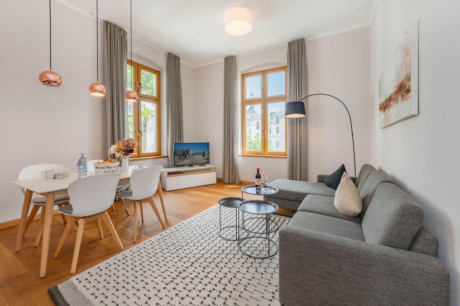 Wohn- und Essbereich mit Sofa, Tisch, Stühlen und Fenstern.
