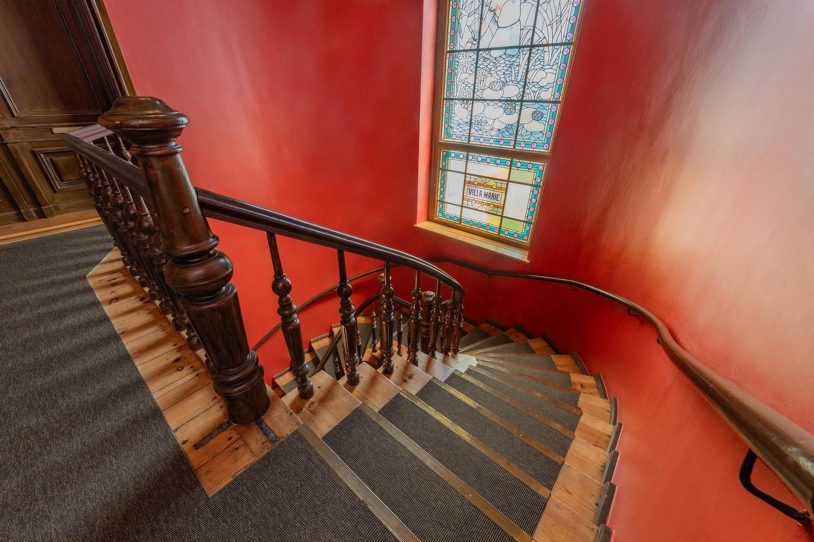 Elegante Treppe mit Holzgeländer und farbigem Glasfenster an roter Wand.