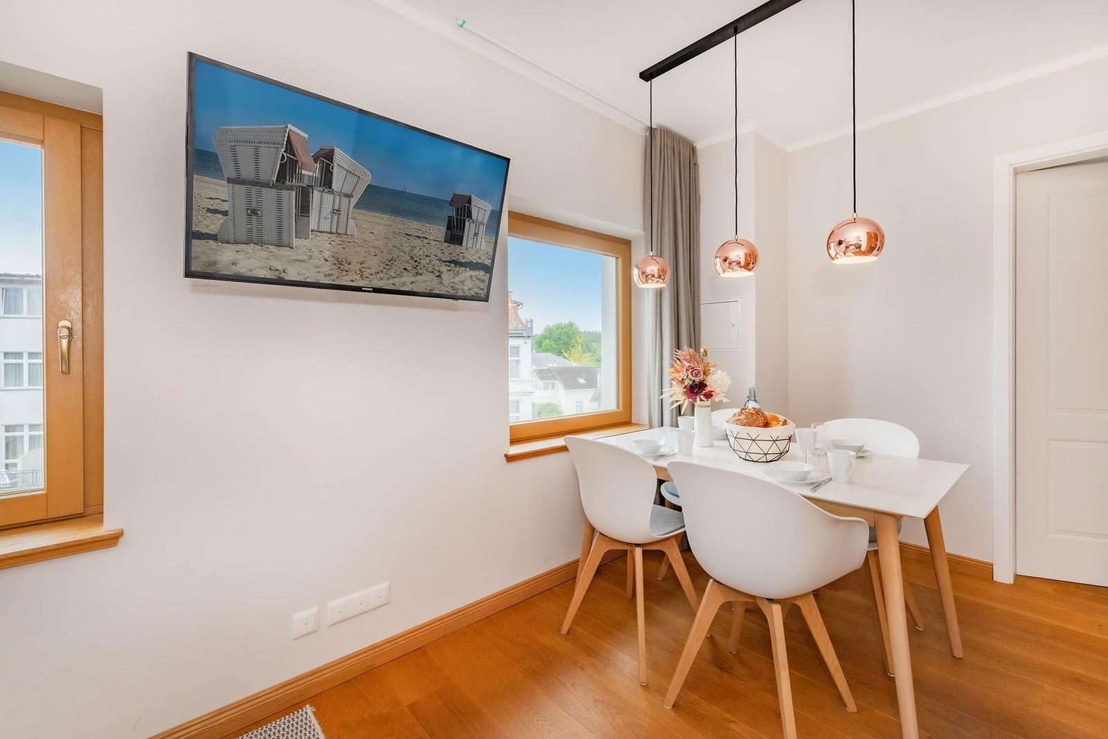 Esszimmer mit Tisch, Stühlen und TV an der Wand. Fenster und Holzboden.