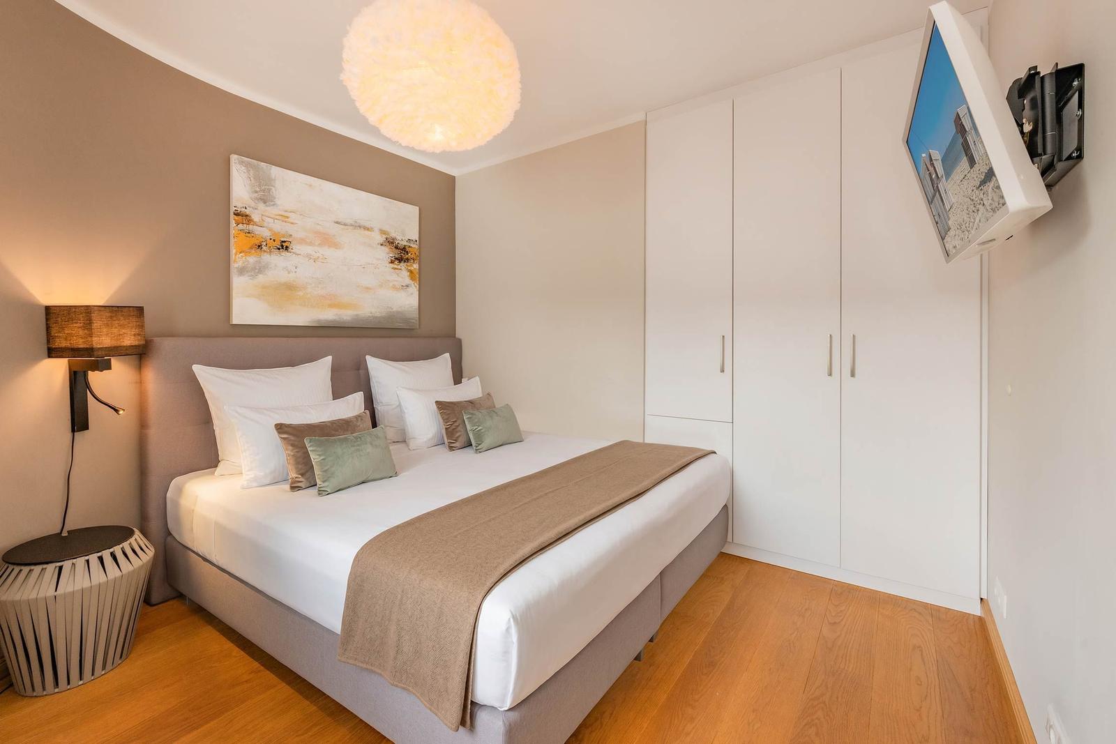 Schlafzimmer mit Doppelbett, Wand-TV und Kleiderschrank.