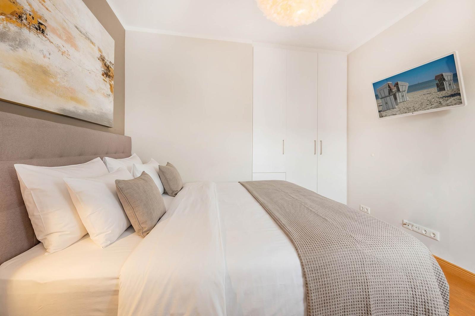 Schlafzimmer mit Bett, Kleiderschrank und Wandbildern.
