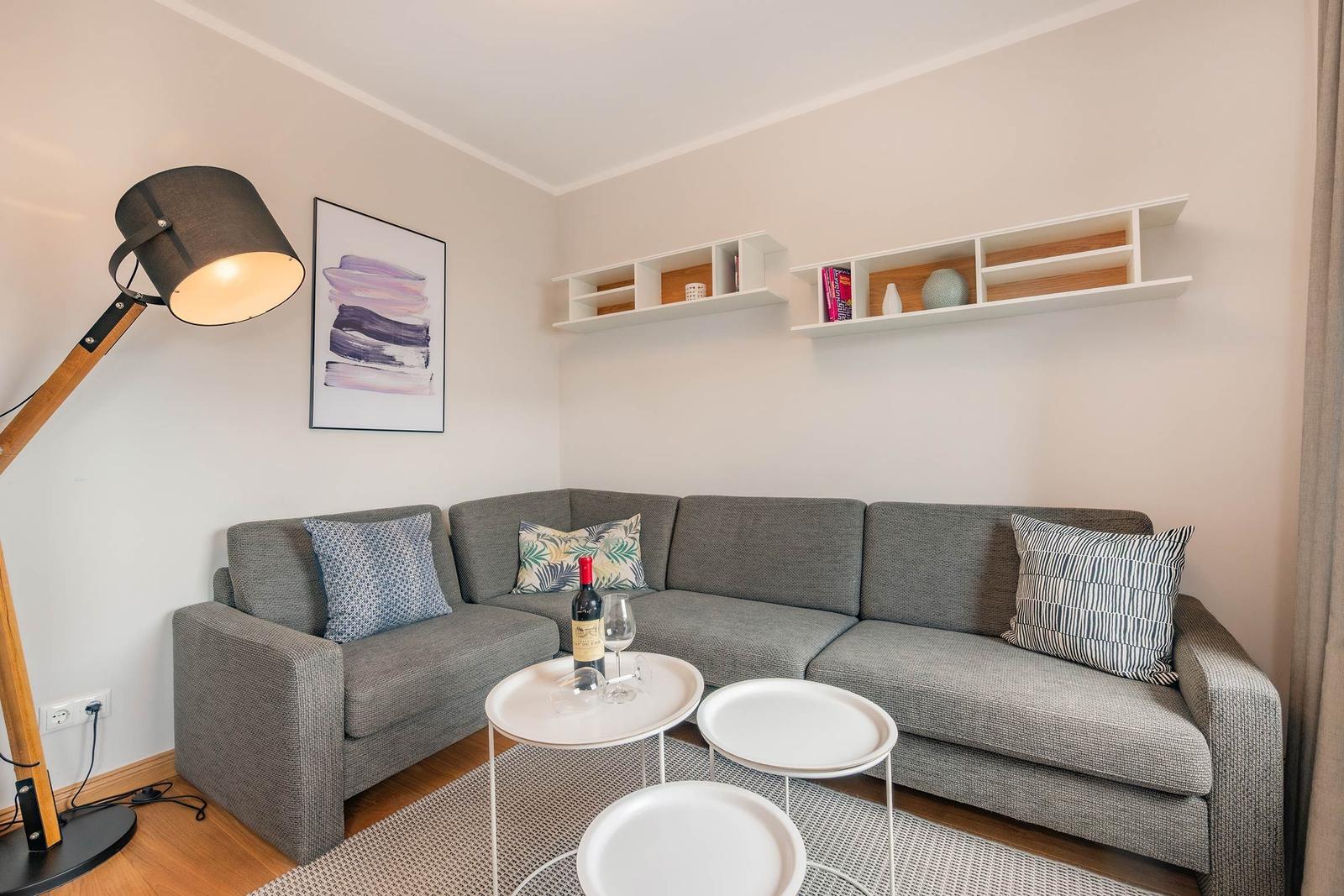 Ein Wohnzimmer mit grauem Sofa, weißen Regalen und einem Stehlampe.