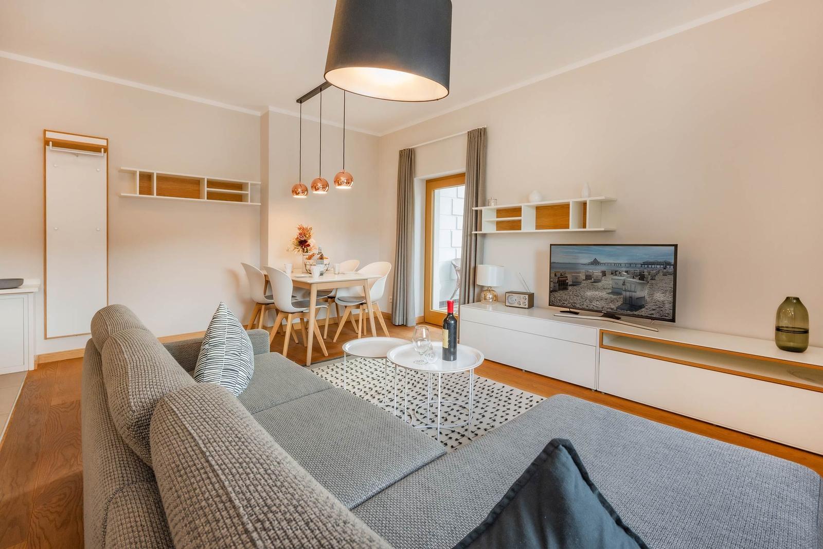 Wohn- und Essbereich mit Sofa, TV und Esstisch. Holzboden und helle Wände.
