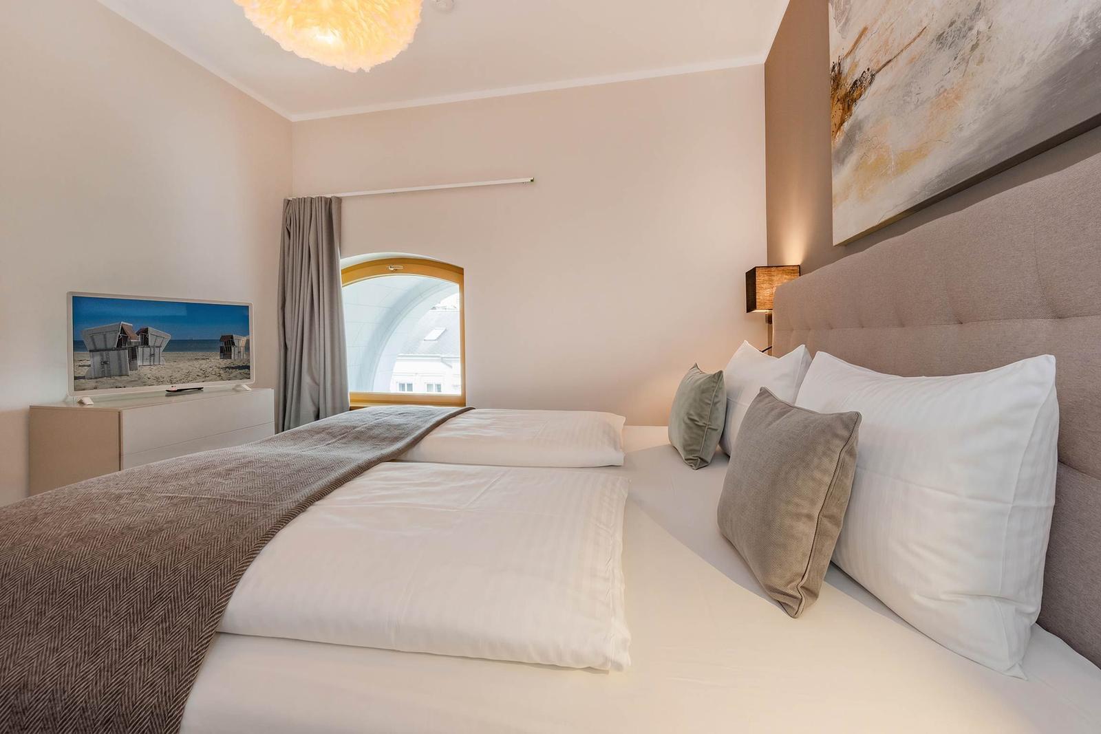 Schlafzimmer mit Doppelbett, Wandbild und Fenster mit Blick auf Gebäude.
