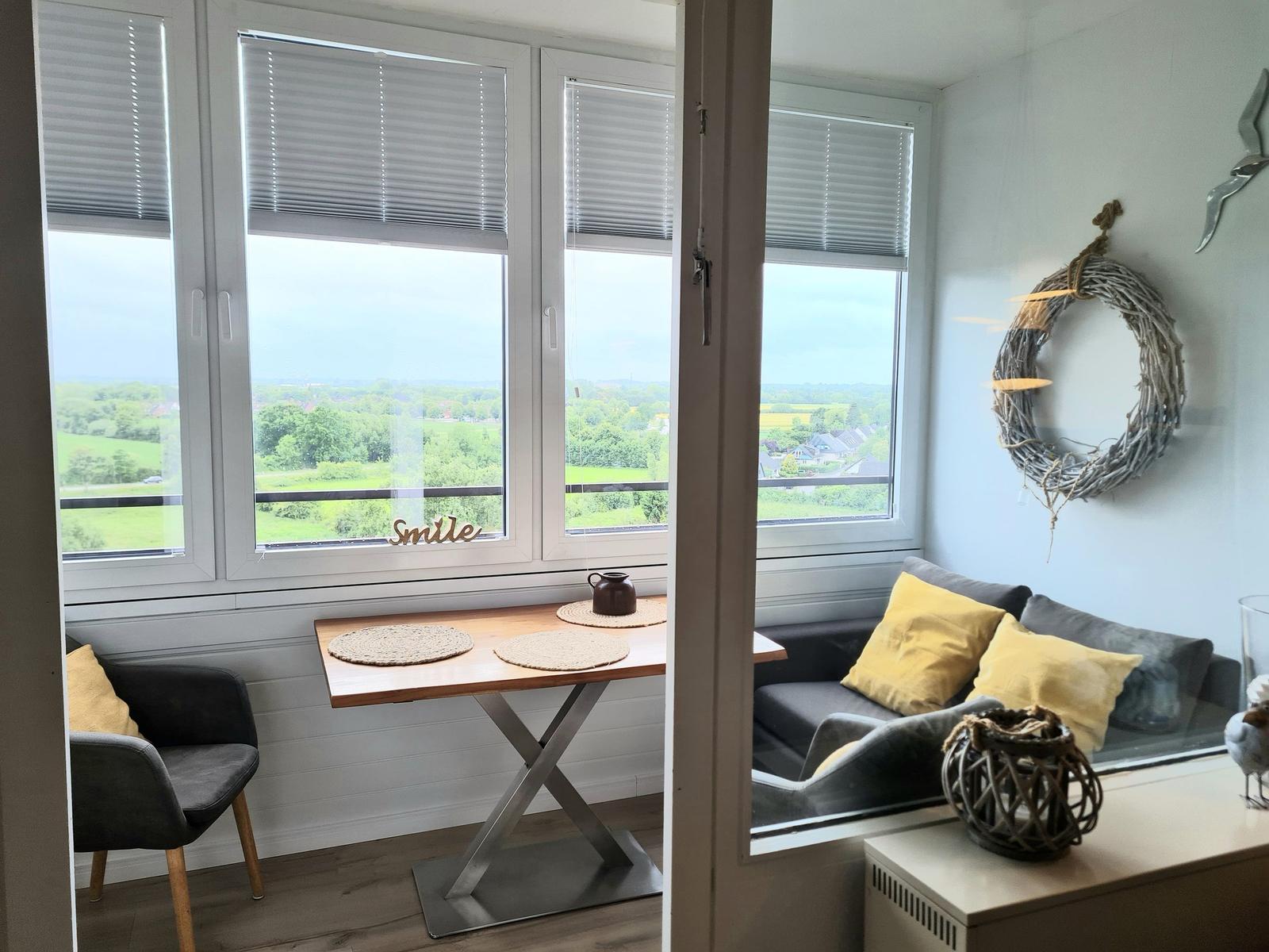 Sitzbereich mit Tisch und Sitzgelegenheiten, Blick auf Landschaft durch Fenster.