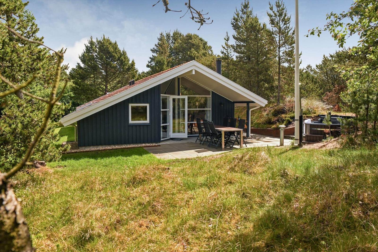 Moderne Holzhütte mit Terrasse, Garten und Grillplatz im Wald.