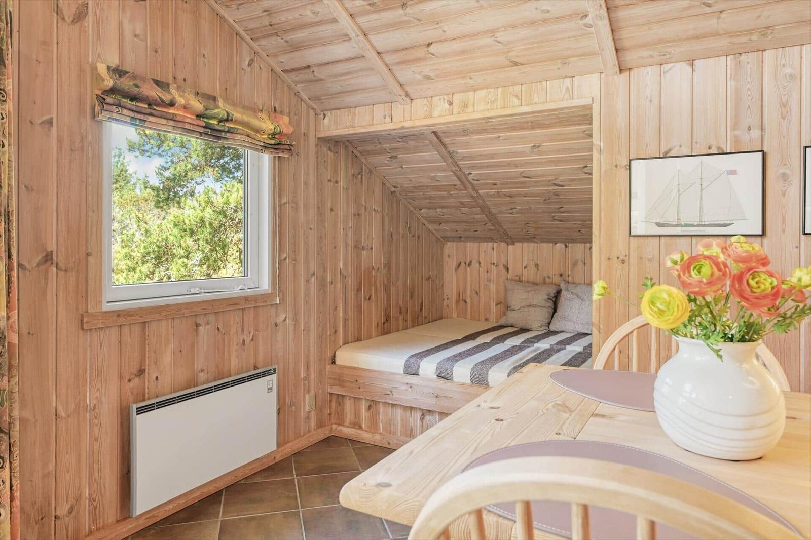 Schlafzimmer mit Holzwand, Bett und Fenster. Tisch mit Blumen und Stühlen.