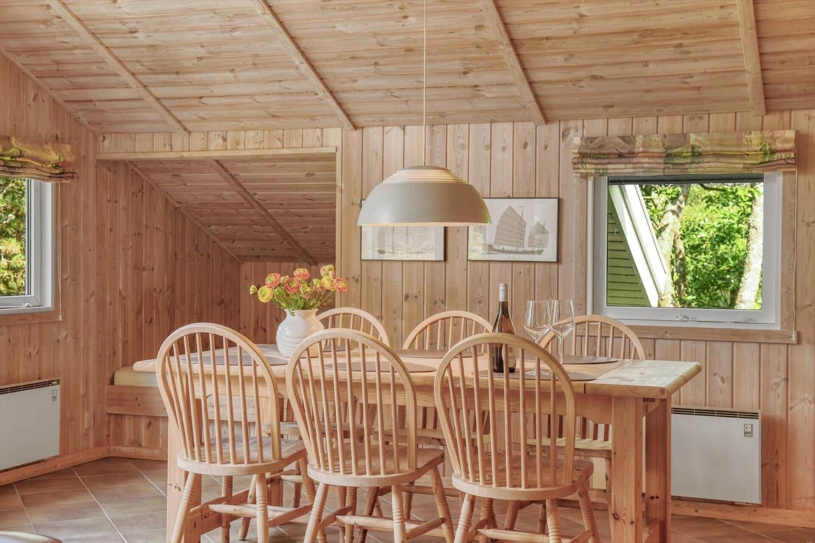 Esszimmer mit Holztisch, Stühlen und Fensterblick auf Grün.