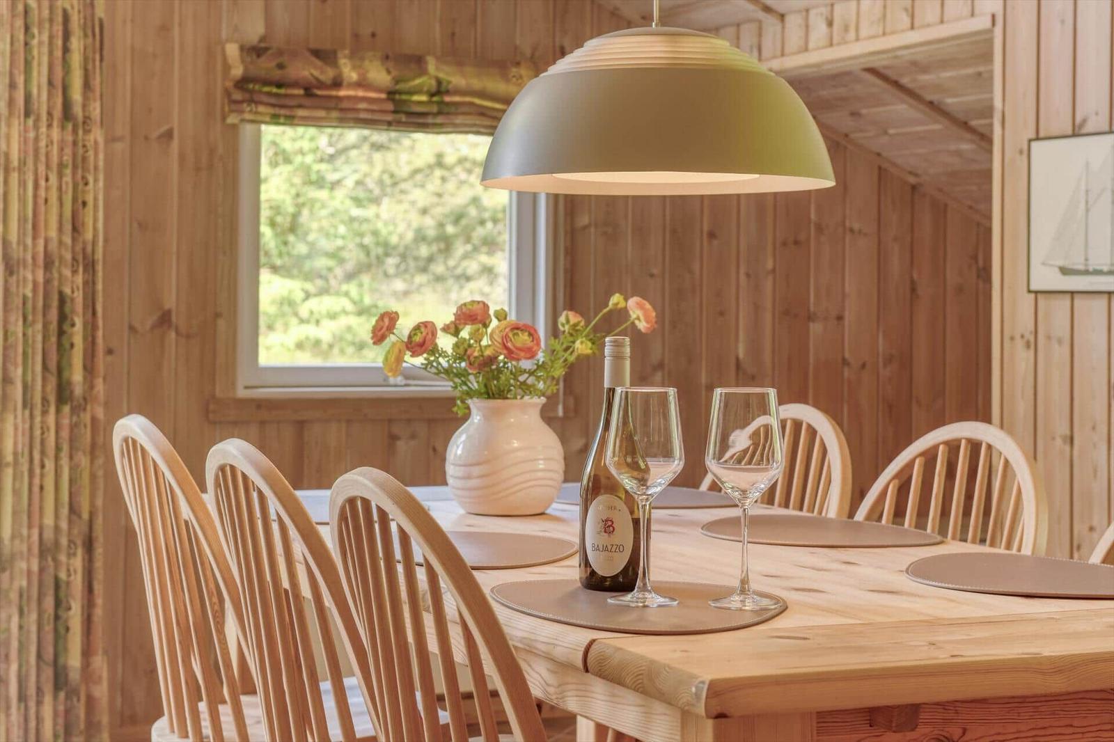 Holztisch mit Stühlen, Wein und Blumen vor Fenster mit Blick auf Grün.