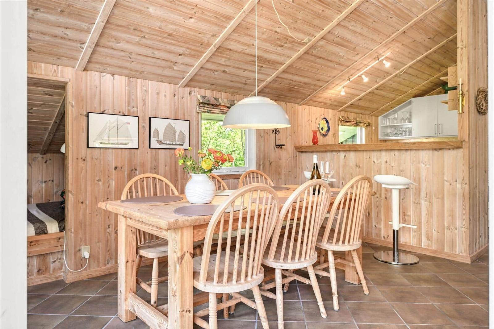 Holzgetäfelte Küche mit Esstisch, Stühlen und Barhocker. Wandbilder und Fenster sichtbar.