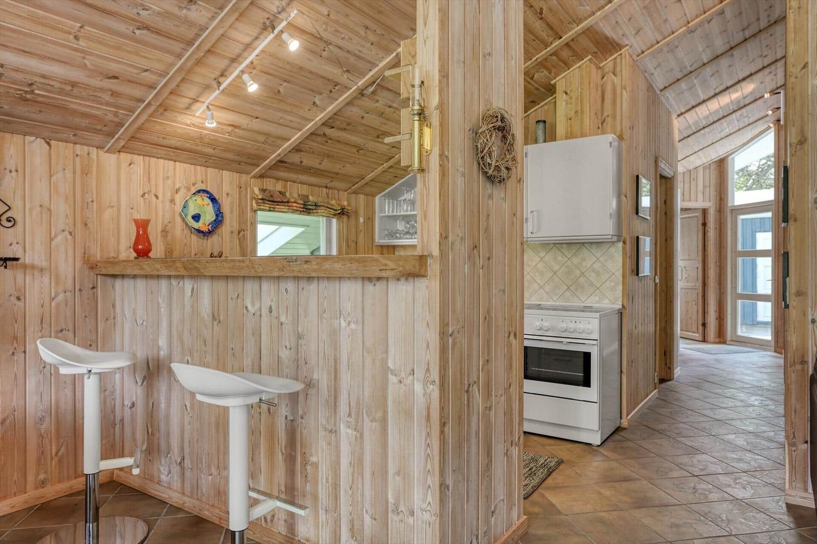 Küche mit weißen Geräten und Holzwand. Barbereich mit zwei Stühlen.