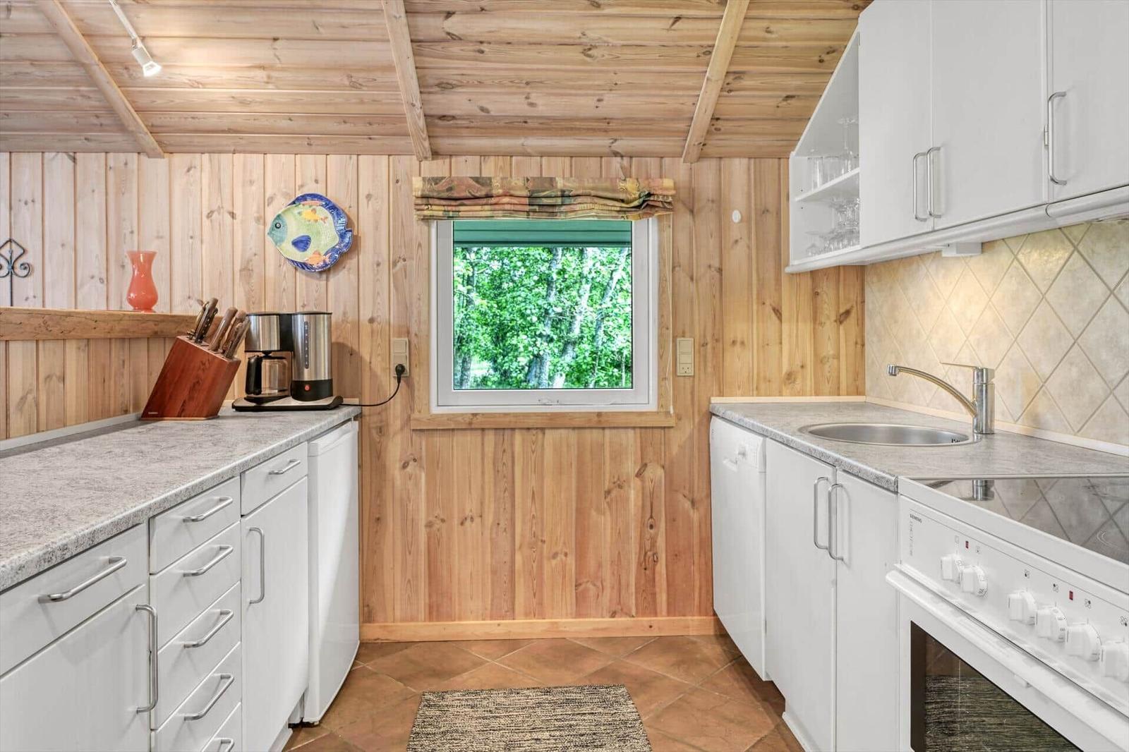Küche mit Holzwänden, Fenster mit Blick auf Bäume, weißen Schränken und Arbeitsplatte.