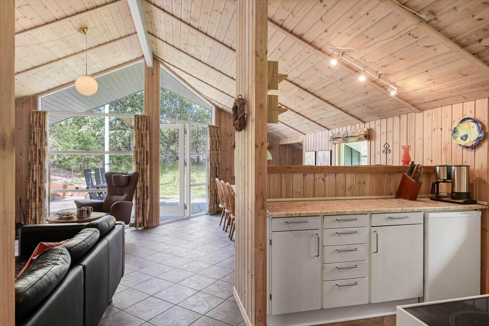 Küche mit Arbeitsplatte, Kühlschrank und Küchenzeile. Wohnbereich mit Sofa und Sicht auf Außenbereich.