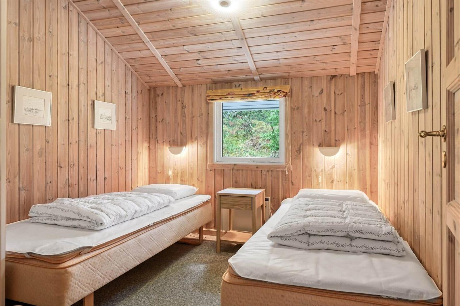 Zwei Betten in einem holzverkleideten Raum mit Fenster und Nachttisch.