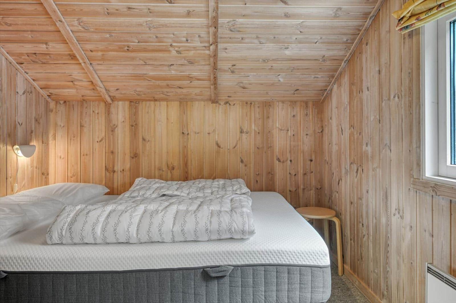Schlafzimmer mit Holzwandverkleidung, Bett und Fenster
