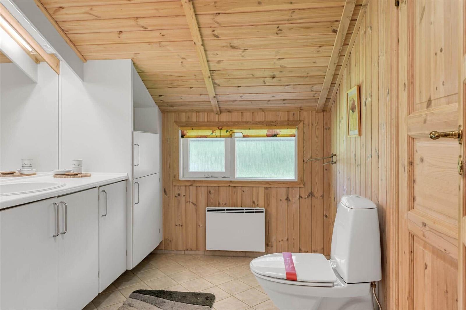Badezimmer mit Holzwand, Toilette, Waschbecken und Fenster mit Gitter.