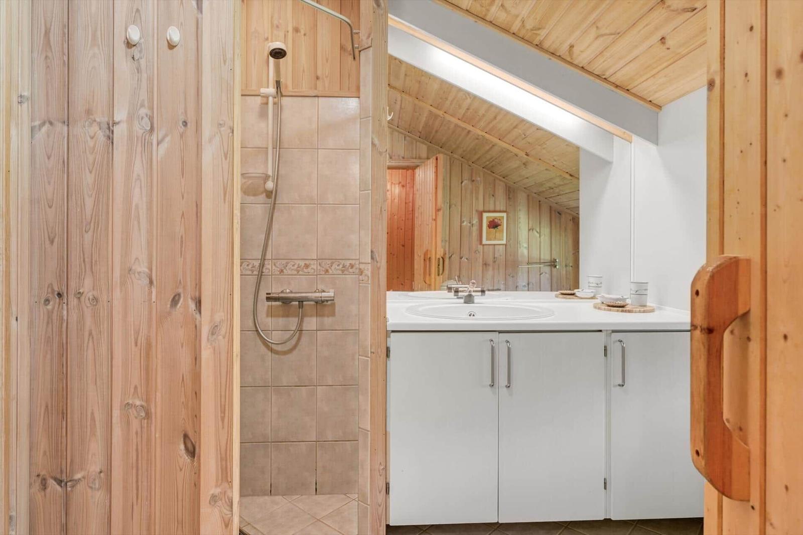 Bad mit Dusche, Waschbecken und Spiegel. Holzwände und -decke.