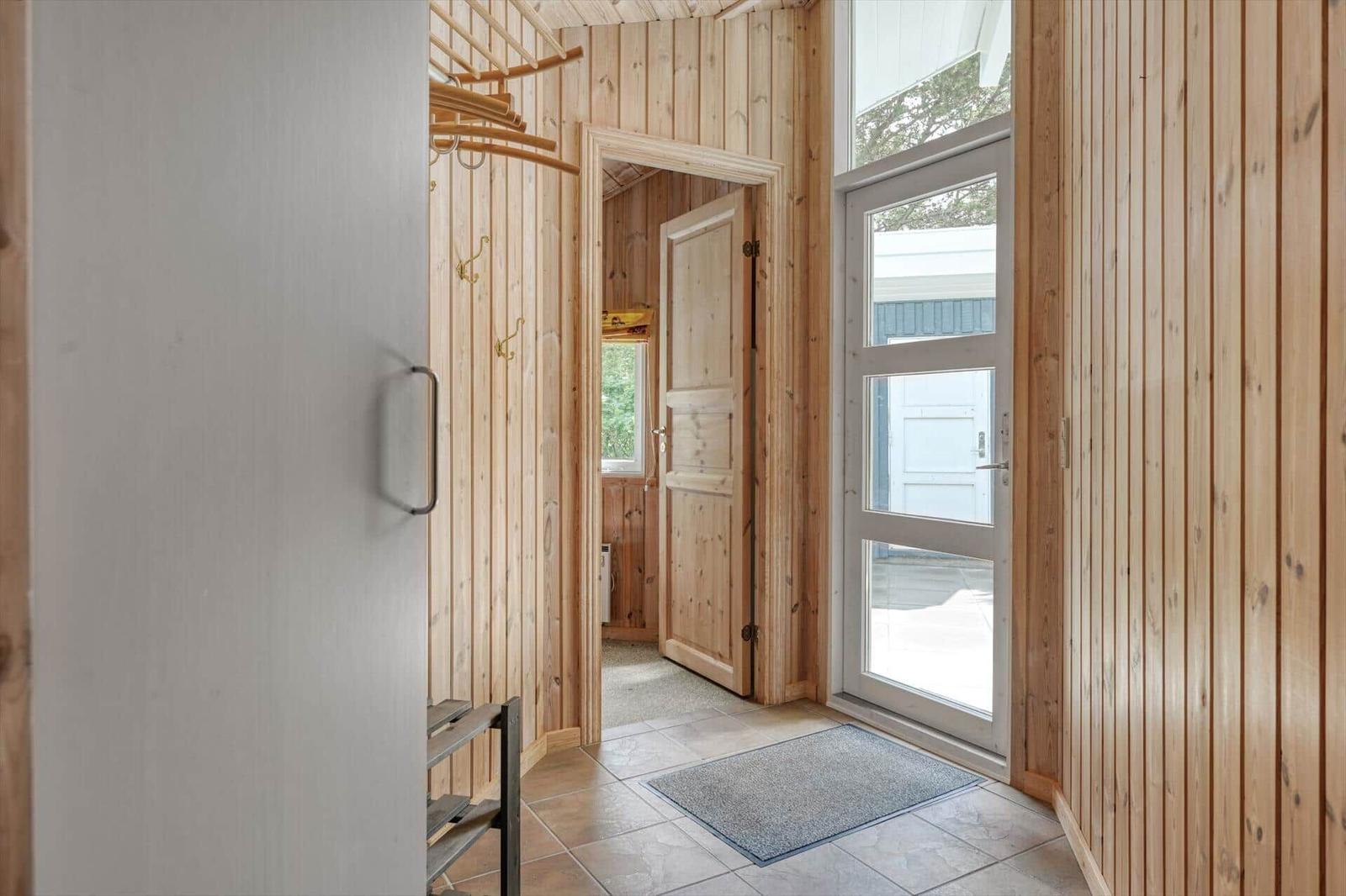 Eingangsbereich mit Holzwand, Tür und Fenster. Fliesenboden und Teppich.