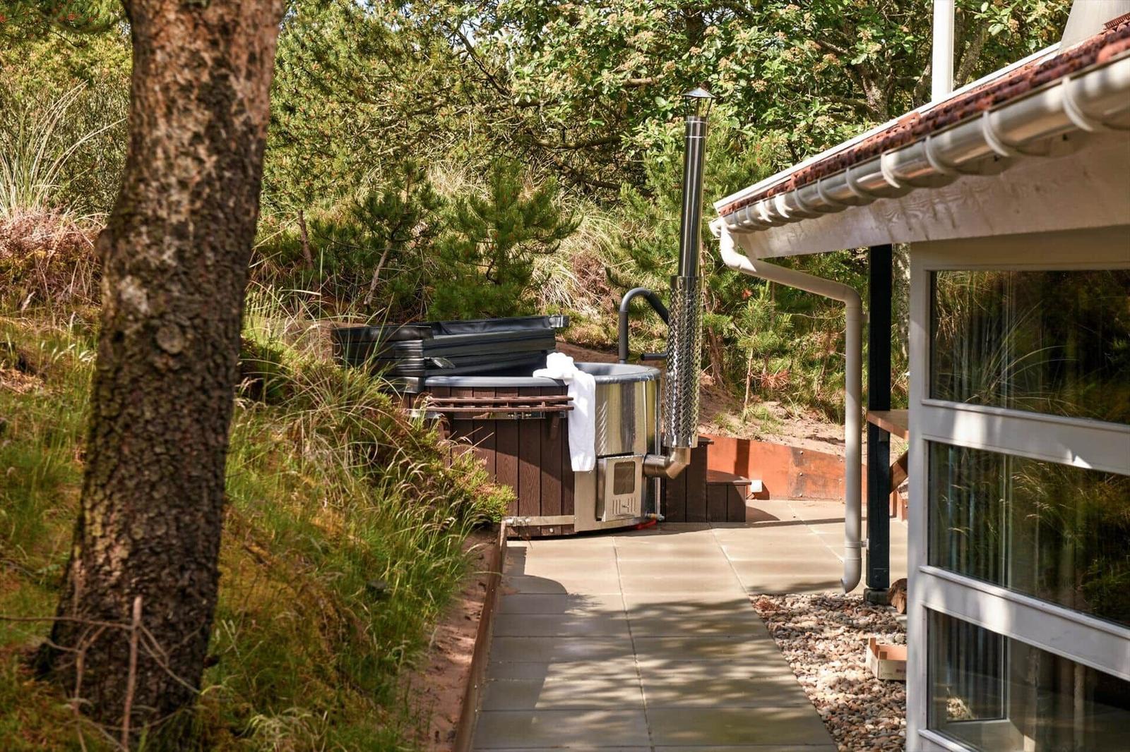 Außenbereich mit Whirlpool und Holzveranda neben modernem Haus in grüner Umgebung.