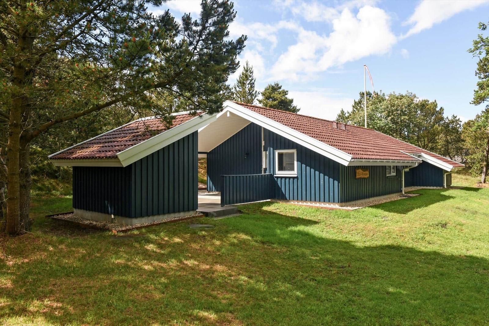 Ein blaues Ferienhaus mit rotem Dach, umgeben von Bäumen und Gras.