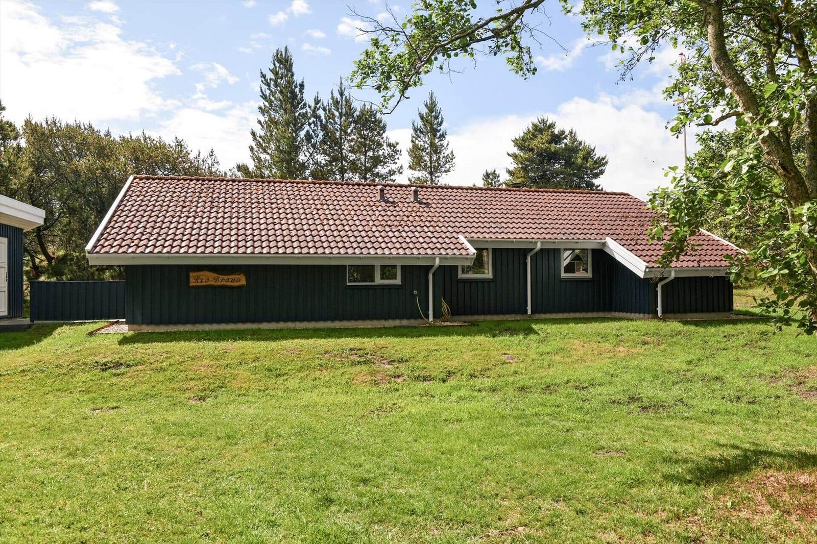 Ein dunkelblaues Haus mit rotem Ziegeldach steht auf einer grünen Wiese unter Bäumen.