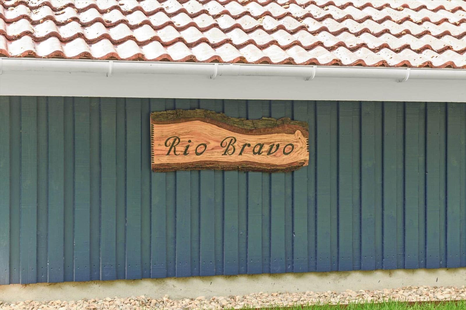 Holzschild mit der Aufschrift Rio Bravo an einer blauen Hauswand unter einem Ziegeldach.